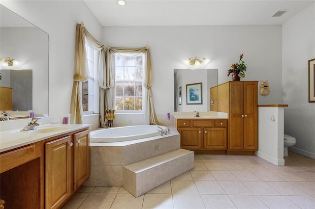 bathroom featuring tiled tub, vanity, tile patterned floors, and toilet