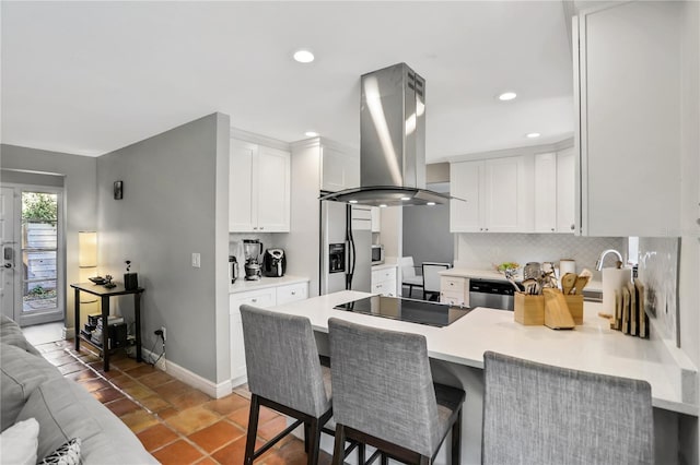 kitchen with white cabinetry, stainless steel appliances, island range hood, a kitchen bar, and kitchen peninsula