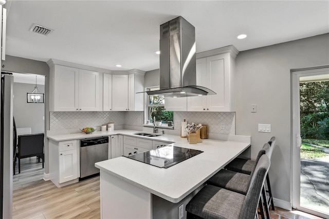 kitchen with a kitchen breakfast bar, kitchen peninsula, island exhaust hood, stainless steel appliances, and white cabinets