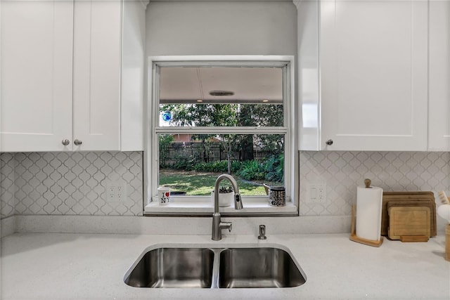 kitchen with white cabinetry, sink, backsplash, and light stone counters