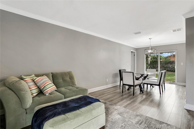 living room featuring wood-type flooring, a chandelier, and crown molding