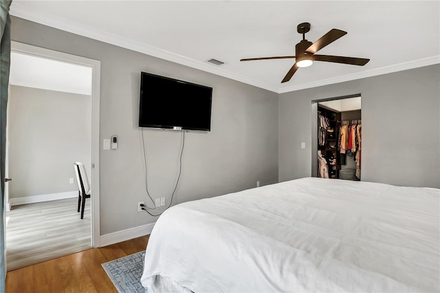 bedroom featuring hardwood / wood-style flooring, ornamental molding, a walk in closet, ceiling fan, and a closet