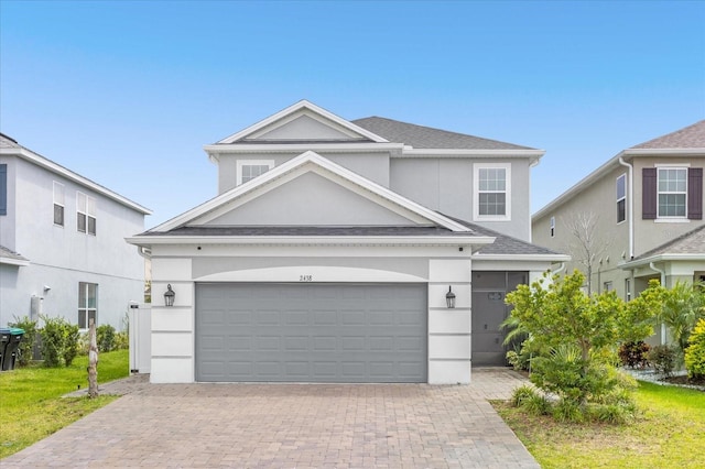 traditional home featuring a garage, a shingled roof, decorative driveway, and stucco siding