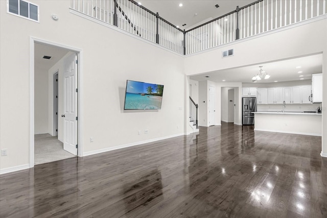 unfurnished living room featuring dark hardwood / wood-style floors, sink, an inviting chandelier, and a towering ceiling