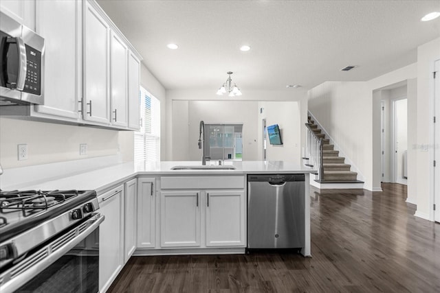 kitchen featuring appliances with stainless steel finishes, sink, white cabinets, dark hardwood / wood-style flooring, and kitchen peninsula