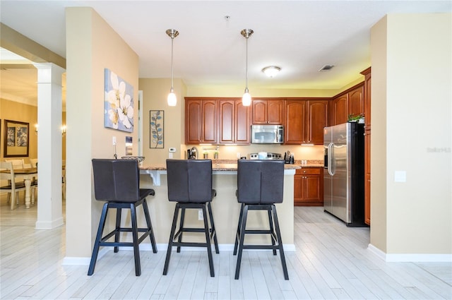 kitchen with stainless steel appliances, decorative columns, light stone counters, light hardwood / wood-style floors, and kitchen peninsula