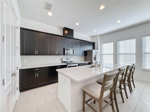 kitchen with a breakfast bar, tasteful backsplash, sink, a kitchen island with sink, and stainless steel appliances