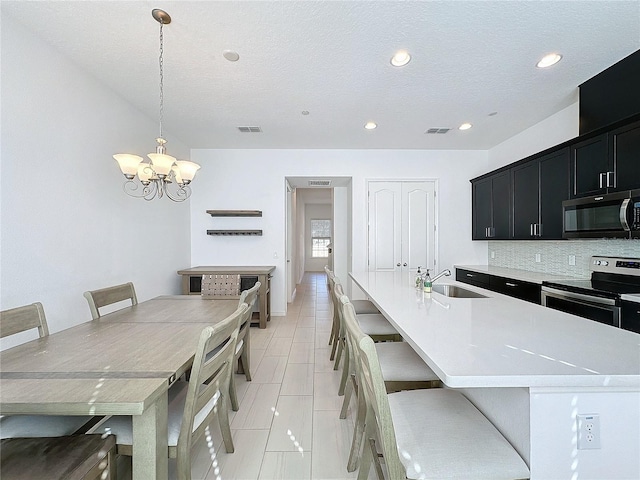 kitchen featuring a breakfast bar, sink, a center island with sink, appliances with stainless steel finishes, and pendant lighting