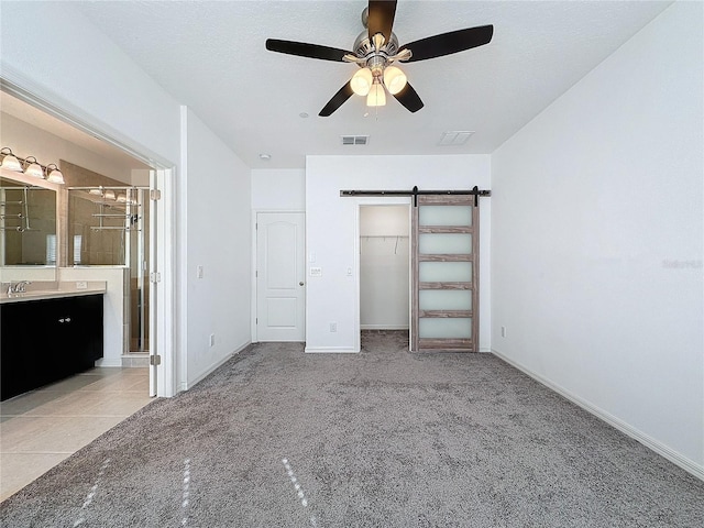 unfurnished bedroom featuring ensuite bathroom, sink, a closet, light colored carpet, and a barn door