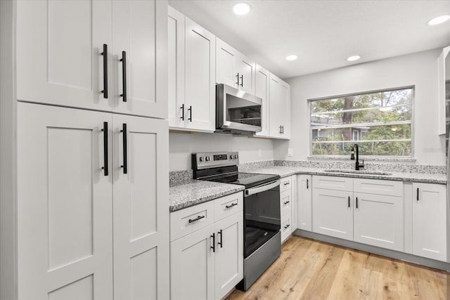 kitchen featuring appliances with stainless steel finishes, white cabinetry, sink, light stone counters, and light wood-type flooring