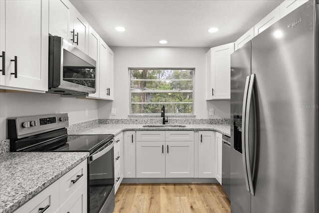 kitchen with sink, stainless steel appliances, white cabinets, and light stone countertops