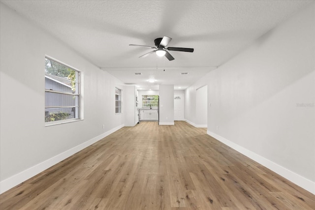 unfurnished living room with light hardwood / wood-style floors, a textured ceiling, and a wealth of natural light