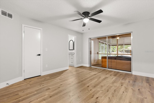 unfurnished bedroom featuring ensuite bath, access to outside, a textured ceiling, and light hardwood / wood-style flooring