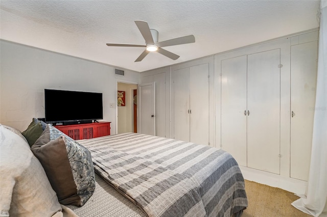 carpeted bedroom with ceiling fan, a textured ceiling, and multiple closets