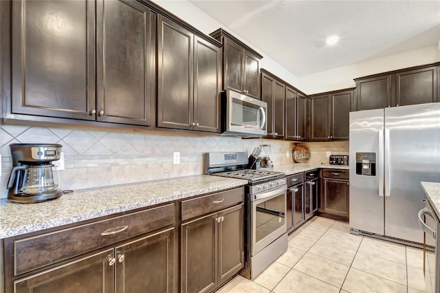 kitchen with appliances with stainless steel finishes, light stone counters, backsplash, and dark brown cabinetry