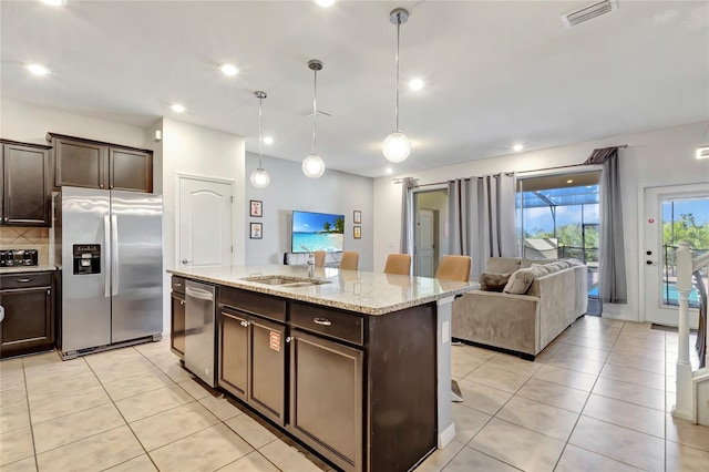 kitchen with sink, appliances with stainless steel finishes, dark brown cabinetry, a center island with sink, and decorative light fixtures