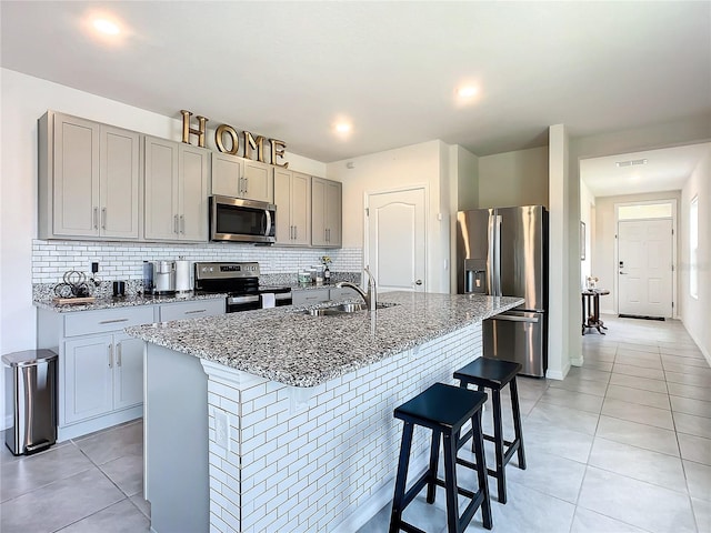 kitchen with light tile patterned flooring, a breakfast bar, sink, appliances with stainless steel finishes, and an island with sink