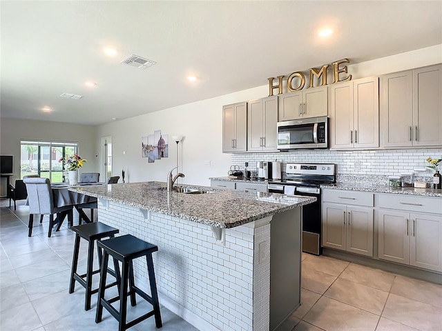 kitchen with a breakfast bar, sink, light stone counters, stainless steel appliances, and a center island with sink