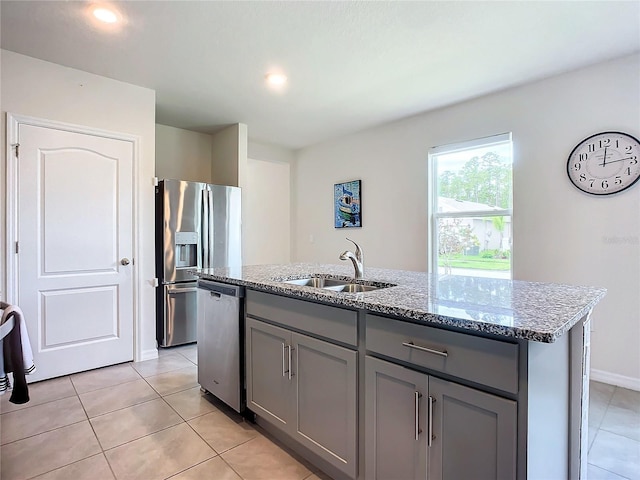 kitchen with light tile patterned flooring, sink, a center island with sink, appliances with stainless steel finishes, and light stone countertops