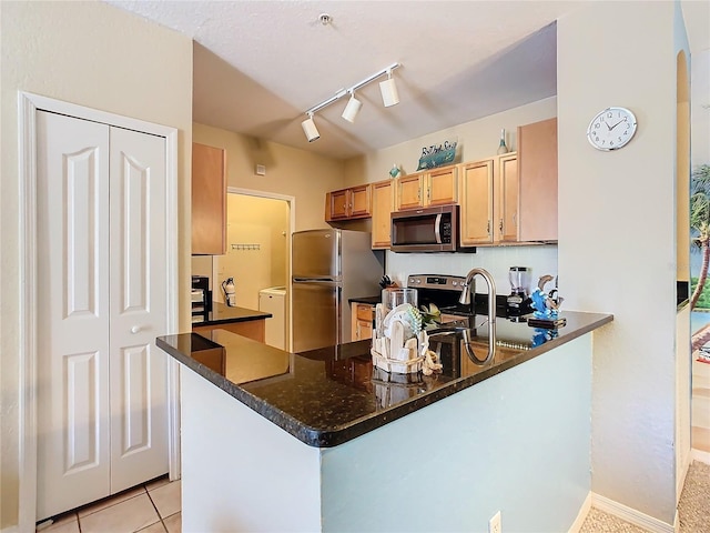 kitchen featuring light tile patterned floors, appliances with stainless steel finishes, track lighting, kitchen peninsula, and dark stone counters