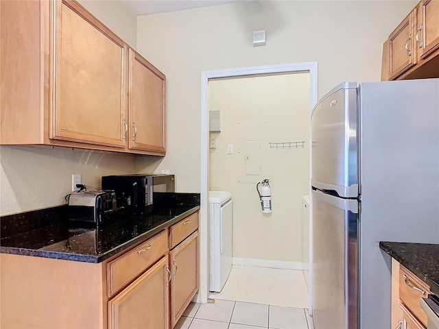 kitchen with light tile patterned flooring, dark stone counters, and stainless steel fridge