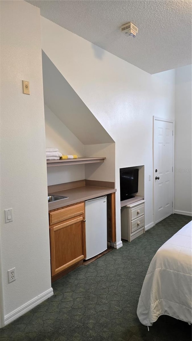 bedroom with sink, refrigerator, dark carpet, and a textured ceiling