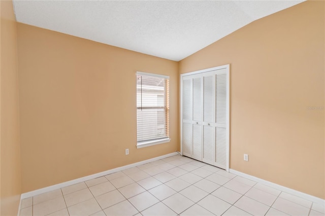 unfurnished bedroom featuring light tile patterned flooring, lofted ceiling, a closet, and a textured ceiling