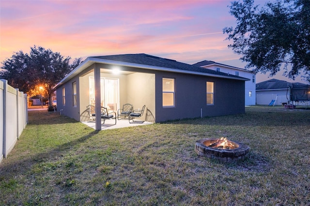 back house at dusk featuring a patio area, a fire pit, and a lawn