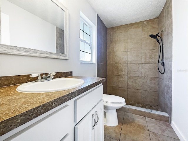 bathroom featuring tile patterned flooring, vanity, tiled shower, toilet, and a textured ceiling