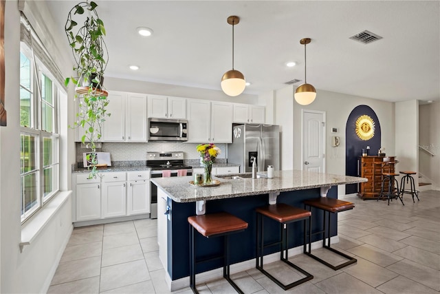 kitchen with stainless steel appliances, light stone countertops, hanging light fixtures, and a center island with sink