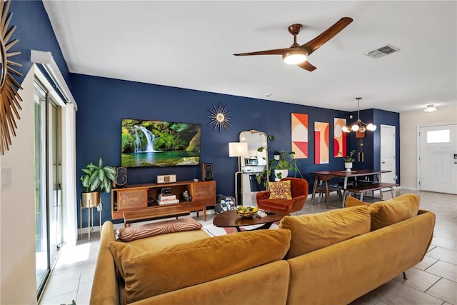 tiled living area with ceiling fan with notable chandelier, visible vents, and baseboards