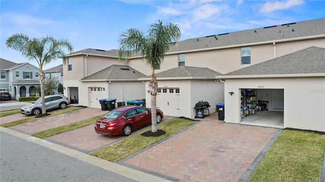 view of property with stucco siding, a shingled roof, an attached garage, a residential view, and driveway