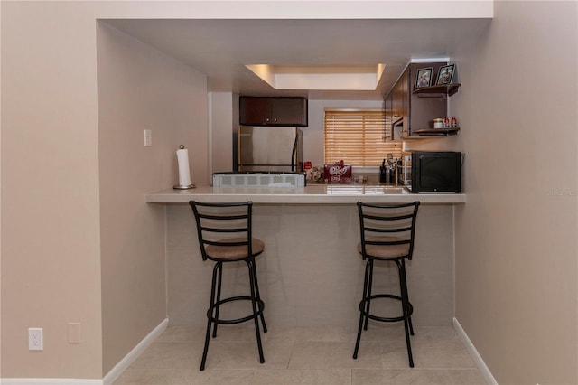 kitchen featuring a breakfast bar, fridge, dark brown cabinetry, a tray ceiling, and kitchen peninsula