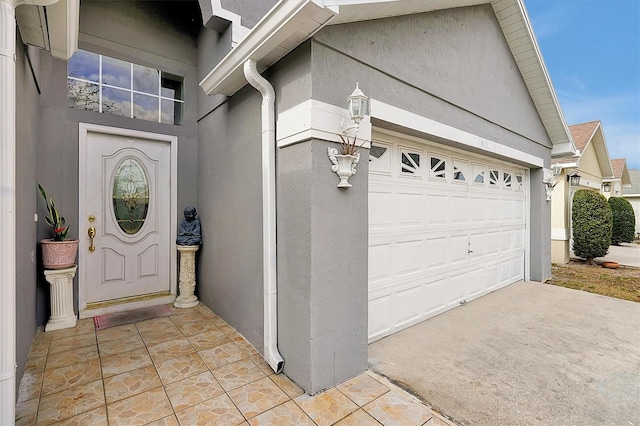 entrance to property featuring a garage, concrete driveway, and stucco siding