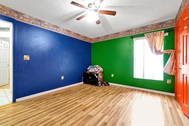 unfurnished room with a textured ceiling, ceiling fan, wood finished floors, and baseboards