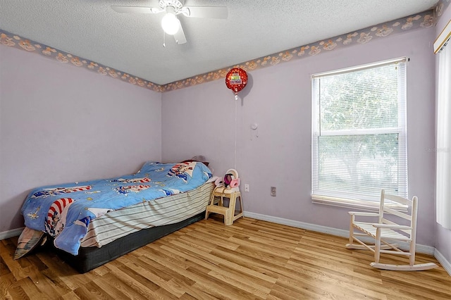 bedroom with a ceiling fan, a textured ceiling, baseboards, and wood finished floors