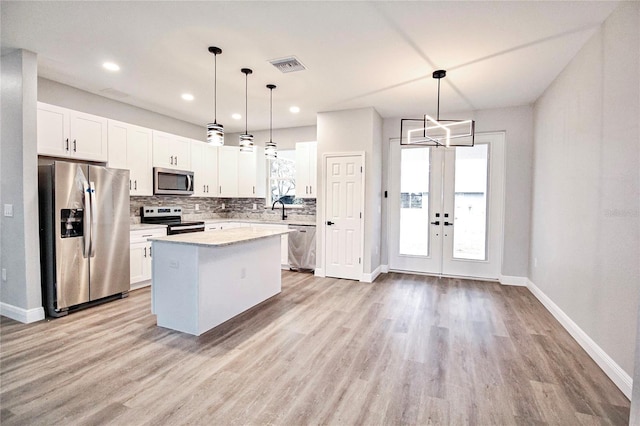 kitchen featuring a kitchen island, appliances with stainless steel finishes, pendant lighting, white cabinetry, and sink