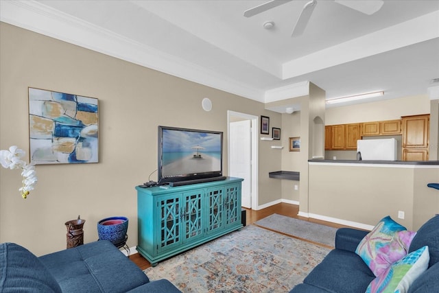 living room with a raised ceiling, ornamental molding, ceiling fan, and light hardwood / wood-style flooring