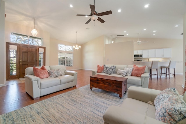 living room with ceiling fan with notable chandelier, wood-type flooring, and high vaulted ceiling