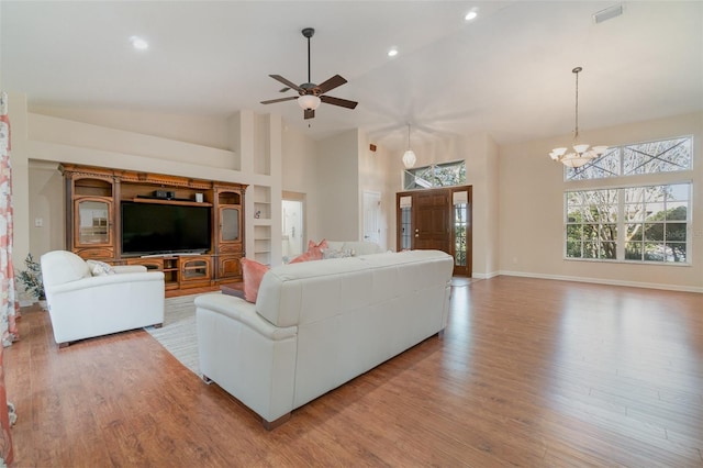 living room with built in shelves, ceiling fan with notable chandelier, high vaulted ceiling, and light hardwood / wood-style floors