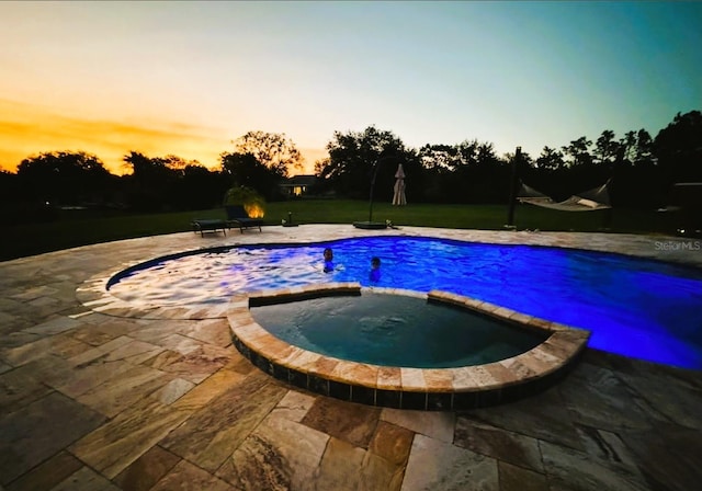 pool at dusk with a patio area and an in ground hot tub