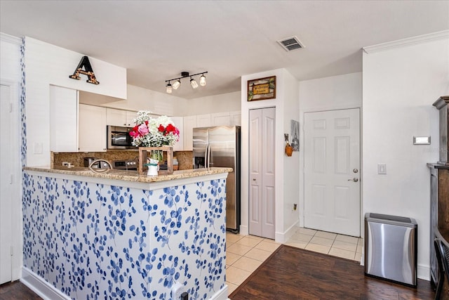 kitchen featuring light tile patterned floors, appliances with stainless steel finishes, white cabinetry, tasteful backsplash, and kitchen peninsula