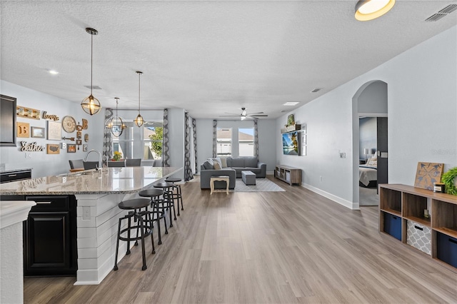 kitchen with sink, light hardwood / wood-style flooring, hanging light fixtures, light stone counters, and a textured ceiling