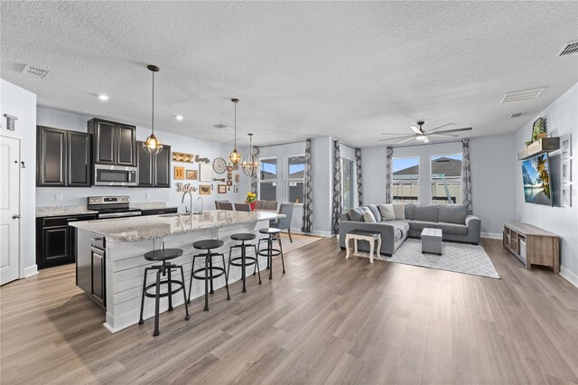 kitchen with a breakfast bar, a textured ceiling, appliances with stainless steel finishes, an island with sink, and pendant lighting