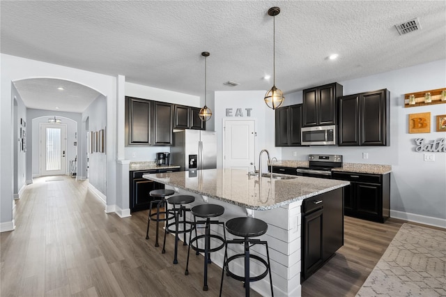 kitchen featuring sink, a kitchen island with sink, hanging light fixtures, stainless steel appliances, and a textured ceiling