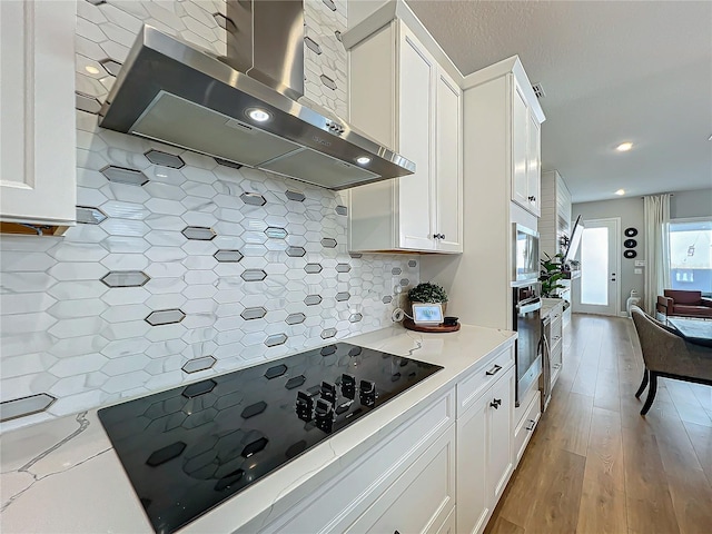 kitchen featuring light stone counters, wall chimney range hood, stainless steel appliances, decorative backsplash, and white cabinets