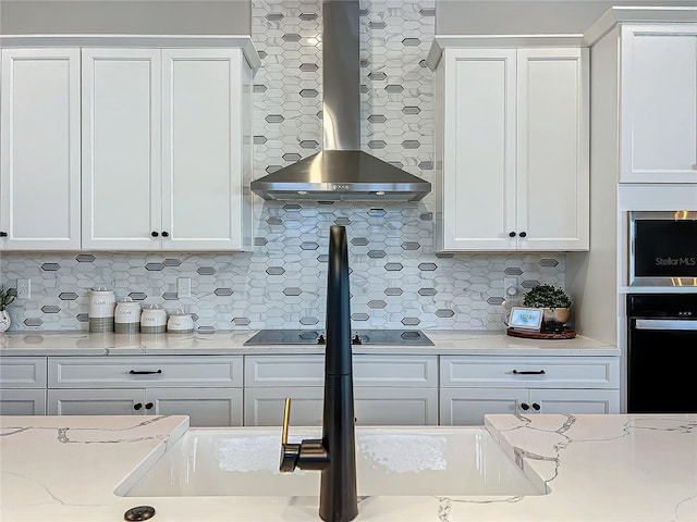 kitchen featuring tasteful backsplash, white cabinetry, black appliances, light stone countertops, and wall chimney range hood