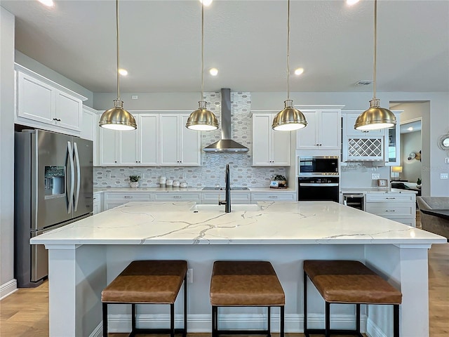 kitchen featuring a spacious island, stainless steel refrigerator with ice dispenser, wall chimney range hood, and decorative light fixtures