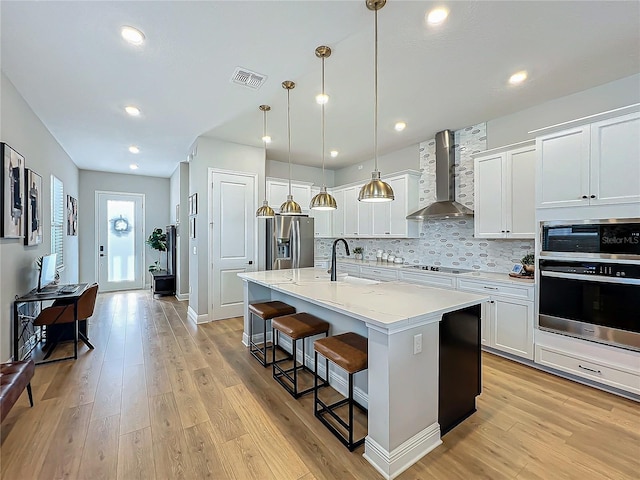 kitchen featuring stainless steel appliances, an island with sink, white cabinets, and wall chimney exhaust hood