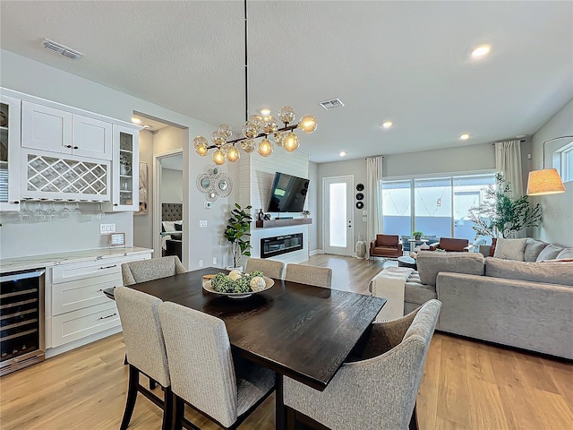 dining area featuring bar area, wine cooler, a fireplace, and light hardwood / wood-style flooring